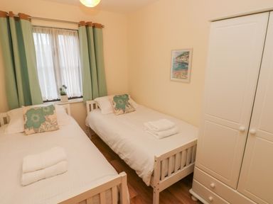 A bedroom with two single beds a white wardrobe and a window with green curtains at 2 Chandlers Yard in Burry Port