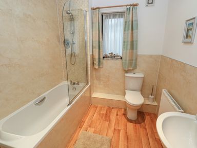 A bathroom with a bathtub shower combination toilet sink and window with curtains at 2 Chandlers Yard in Burry Port