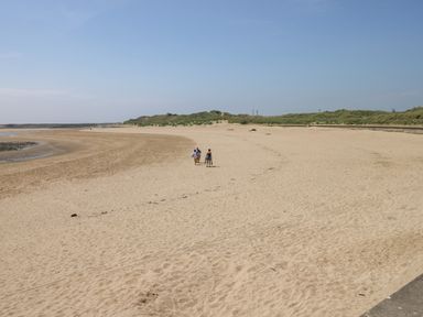 A wide sandy beach with three people walking towards dunes at 2 Chandlers Yard in Burry Port