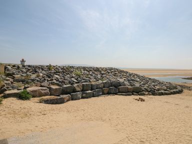 A sandy beach with large rocks forming a seawall and a small lighthouse in the background at 2 Chandlers Yard in Burry Port