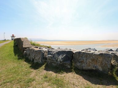 Rock wall along a grassy path leading to a small lighthouse near a sandy beach at 2 Chandlers Yard in Burry Port