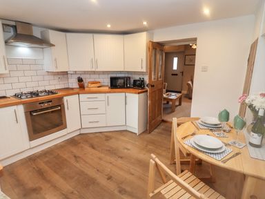 A kitchen with white cabinets wooden countertops and a dining table set for two at The Cottage in Tetbury