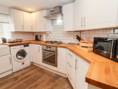 A kitchen with white cabinets wooden countertops a washing machine oven microwave and bread on a cutting board at The Cottage in Tetbury
