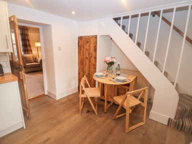 A small dining area with a wooden table and chairs under stairs next to a door leading to a living room at The Cottage in Tetbury