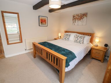 A bedroom with a wooden bed frame bedside tables lamps and wall art at The Cottage in Tetbury