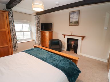 A bedroom with a bed a wooden wardrobe a chest of drawers a chair a fireplace and a window at The Cottage in Tetbury