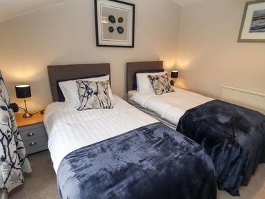 A bedroom with two single beds with floral cushions and dark blue throws at The Cottage in Tetbury