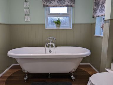 A bathroom with a white clawfoot bathtub under a window with a plant on the sill and framed leaf prints on the wall at The Cottage in Tetbury