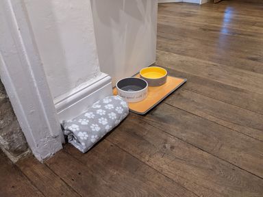A pet feeding area with two bowls and a paw print cushion on a wooden floor at The Cottage in Tetbury