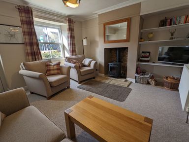 A living room with armchairs a wood stove a television and bookshelves at The Cottage in Tetbury