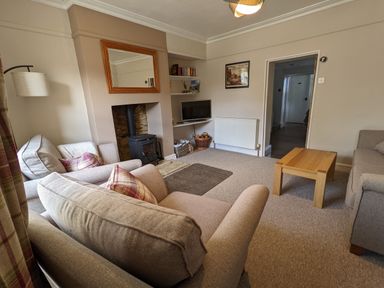 A living room with two sofas a wooden coffee table a wood stove and a television on shelves at The Cottage in Tetbury