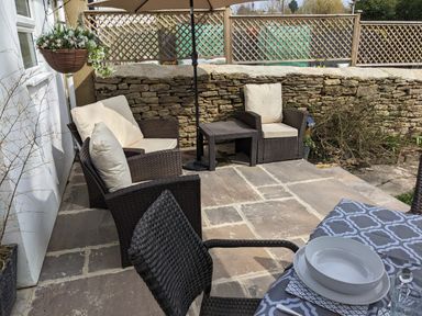 An outdoor patio with wicker chairs and a table set with dishes and cutlery at The Cottage in Tetbury