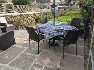An outdoor patio with a table set for four with dishes and glasses and brown wicker chairs at The Cottage in Tetbury