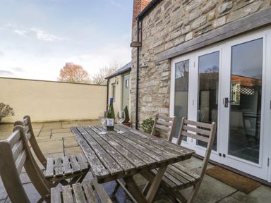 An outdoor patio with a wooden table and chairs next to a stone wall with glass doors at Magnolia Barn in Mark