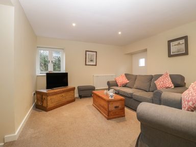 A sitting room with grey sofas wooden chests a television and framed pictures on the walls at Magnolia Barn in Mark