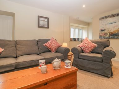 A living room with a grey sofa and armchair with red patterned cushions a wooden coffee table with teapot cups and a small jar a lamp between the sofa and armchair and artwork on the walls at Magnolia Barn Mark