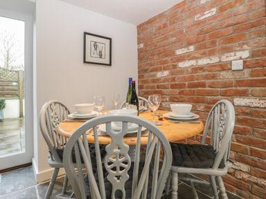 A dining area with a round wooden table set with plates glasses and bottles against a brick wall at Magnolia Barn in Mark