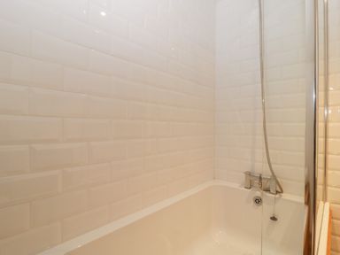 A bathroom with a white tiled wall and a bathtub with a showerhead at Magnolia Barn in Mark