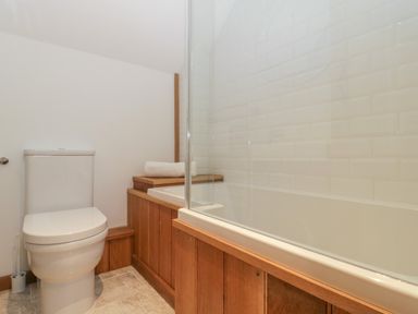 A bathroom with a toilet and a bathtub with wooden paneling and white tiled wall at Magnolia Barn in Mark