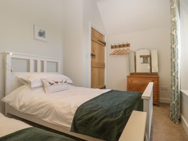 A bedroom with two white beds green throws wooden door wooden dresser with triple mirror and coat rack at Magnolia Barn Mark