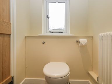 A small bathroom with a closed toilet seat under a window and a toilet paper holder on the wall at Magnolia Barn in Mark