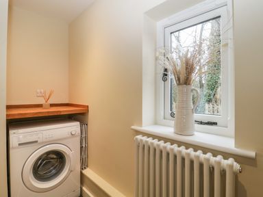 A laundry room with a washing machine a wooden shelf and a vase with dried flowers on the window sill at Magnolia Barn in Mark