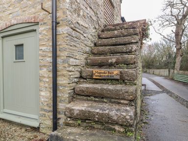 An exterior stone staircase next to a green door with a sign indicating Magnolia Barn entrance to the rear at Magnolia Barn in Mark