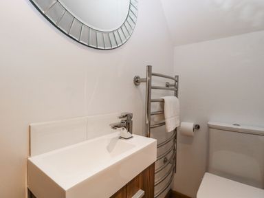 A bathroom with a white sink and tap a toilet a towel rail with a towel and a round mirror at Magnolia Barn in Mark
