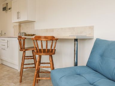 A kitchen area with wooden chairs and a blue sofa at The Stables in Crowcombe