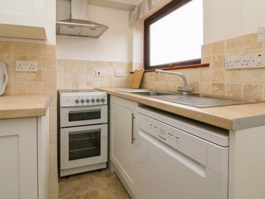 A kitchen corner with a stove a sink a dishwasher and tiled backsplash at The Stables in Crowcombe