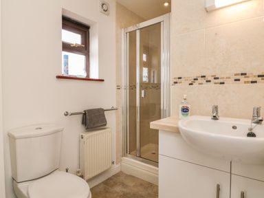 A bathroom with a toilet, towel on a rail, a shower cubicle, a sink with hand soap and a small window at The Stables in Crowcombe