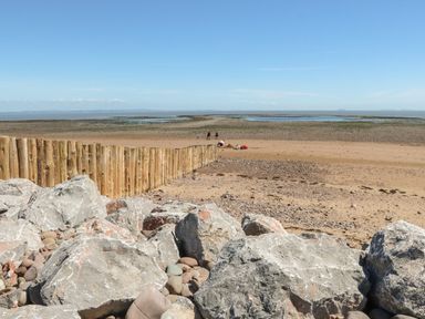 A beach scene with large rocks and wooden posts along the sand with people in the distance at The Stables in Crowcombe