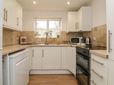 A kitchen with white cabinets a dishwasher an oven a microwave and a window with a curtain at The Outlook in Crowcombe