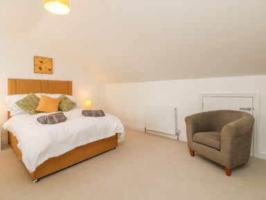 A bedroom with a double bed with pillows and towels a brown armchair and a small door at The Outlook in Crowcombe
