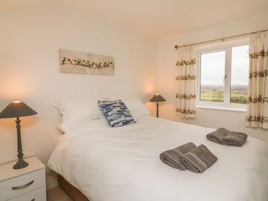 A bedroom with a double bed two bedside tables with lamps a window and bird-themed curtains at The Outlook in Crowcombe