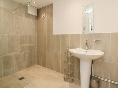 A bathroom with a pedestal sink a small round mirror a metal rack and a walk-in shower at The Outlook in Crowcombe