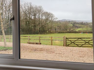 A window view of a gravel path a wooden fence trees and green hills at The Outlook in Crowcombe