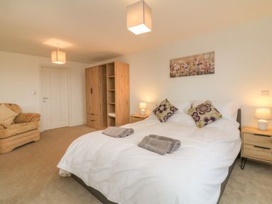 A bedroom with a double bed with pillows and towels two bedside tables with lamps a wooden wardrobe and an armchair at The Outlook in Crowcombe