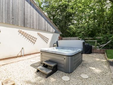 An outdoor hot tub with steps on a gravel surface beside a building with wooden and white walls at The Outlook in Crowcombe