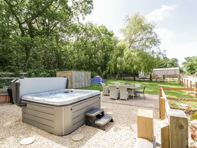 An outdoor area with a hot tub on gravel and a patio table with chairs on a lawn at The Outlook in Crowcombe