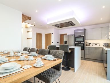 A dining table set with dishes and glasses next to a kitchen with modern appliances and bar stools at Valley View in Mullion