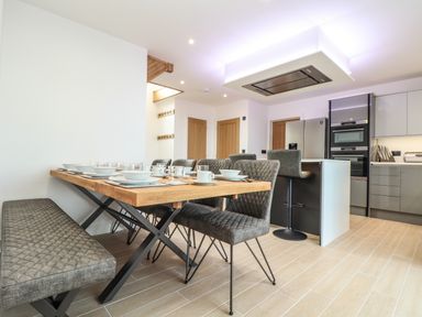 A kitchen and dining area with a wooden table set with plates and glasses at Valley View in Mullion
