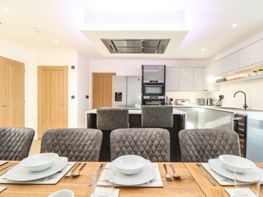 A dining table set with plates and bowls in a kitchen with modern cabinets and appliances at Valley View in Mullion