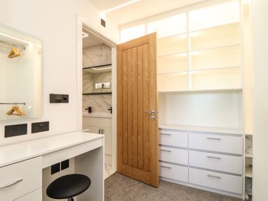 A dressing room with a white vanity desk and stool next to an open wooden door showing a bathroom at Valley View in Mullion