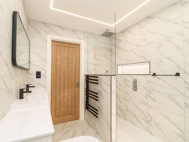 A bathroom with a wooden door double sink mirror shower area and heated towel rail at Valley View in Mullion