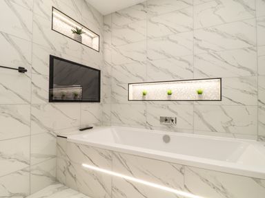 A bathroom with a bathtub surrounded by marble tiles and recessed shelves holding plants at Valley View in Mullion