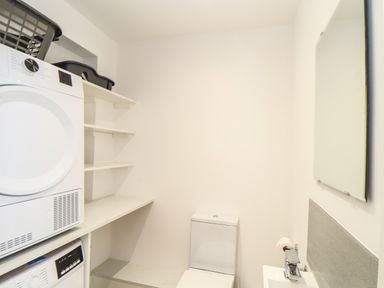 A laundry room with stacked washer and dryer shelves a toilet and a sink at Valley View in Mullion