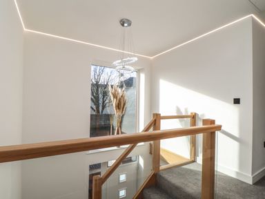A staircase with wooden handrails and glass panels next to a large window with dried plants in a vase at Valley View in Mullion
