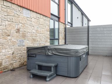 An outdoor hot tub with a cover and steps on a tiled patio next to a stone and wood wall at Valley View in Mullion