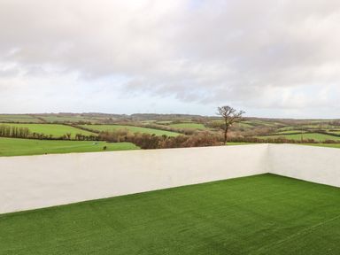A rooftop area with artificial grass and white walls overlooking green fields and distant wind turbines at Valley View in Mullion